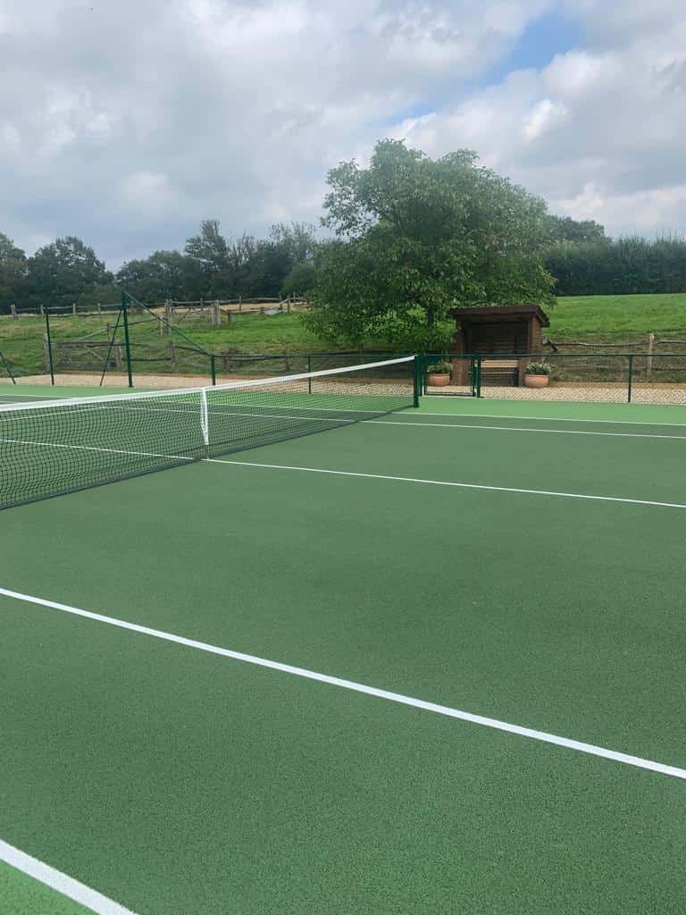 This is a photo of a new tennis court showing the actual tennis court surface which is green with white lines, and also the service line and net, and the green tapered drop fencing.